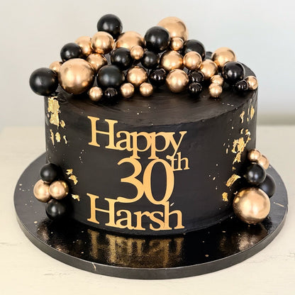 chocolate cake with gold and black decorations and 'Happy 30th Harsh' text on a white background